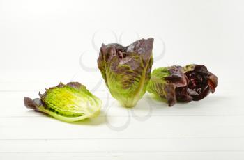 two and half heads of fresh lettuce on white wooden background