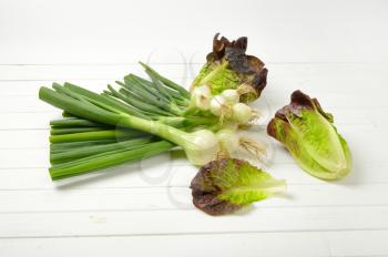 bunch of spring onions and heads of fresh lettuce on white wooden background