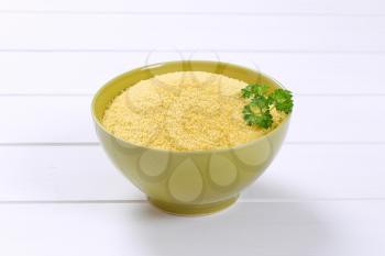 bowl of raw couscous on white wooden background