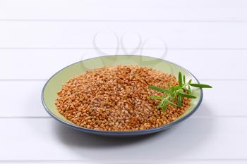 plate of raw buckwheat groats on white wooden background