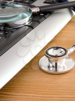 stethoscope and laptop with magnifier on wooden table