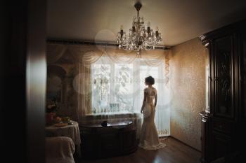 The bride in a wedding dress is by the window.