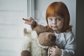 Girl with a toy sitting on the windowsill.