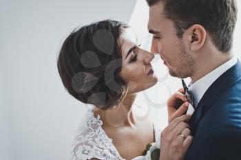 Young husband and wife gently kiss each other on the bright background of the window.