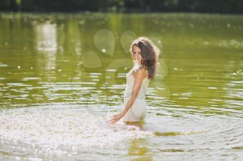 Girl squirts water standing waist-deep in the lake.