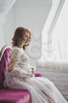 Pregnant girl in a semitransparent negligee sitting on the sofa.