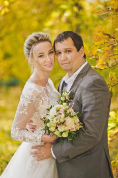 Close-up portrait of the bride and groom on a background of yellowing autumn leaves of the trees.