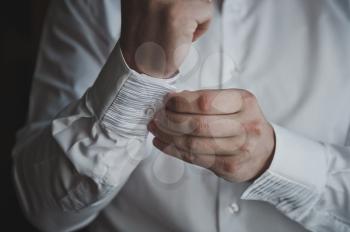 The process of fastening the buttons on his white shirt.