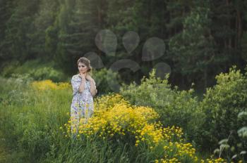 Beautiful girl in a long light dress in a clearing with yellow flowers.