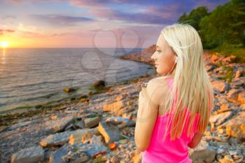 young blond woman standing at sunset on the sea skruzhkoy coffee and headphones. summer evening