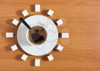 Cup of coffee with saucer and sugar like a clock on a wooden brown table, top view 