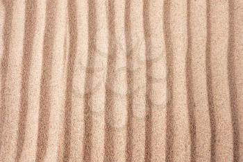 Red dry sand surface with grooves and wavy lines close-up top view with shallow depth of field nature background