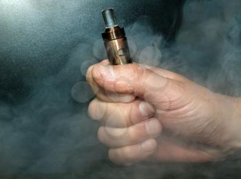 Hand with an electronic cigarette in the clouds of steam on a dark background