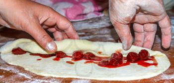 The hands of the confectioner close up with wrapping a roll with cherries