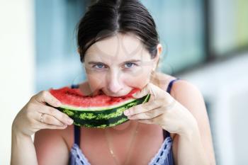 Pretty young woman holding and biting a fresh juicy watermelon. Shallow depth of field. Selective focus on the model's face.