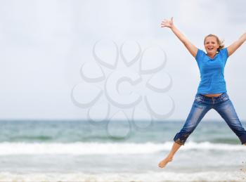 Happy woman jumping on the beach against the sea and cloudless sky. Selective focus. Space for text. Shallow depth of field. Focus on model.