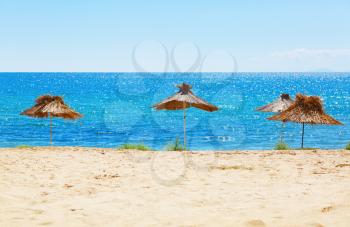 Straw beach umbrellas on a background of  calm sea on a bright sunny day. Selective focus on the parasols. Shallow depth of field. 