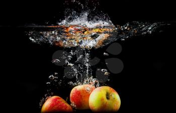 Apples falling into the water with splashes and bubbles. Photo on black background. High speed photography.