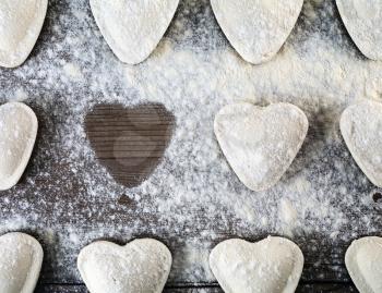 Heart shaped ravioli sprinkle with flour, on wooden background. Cooking dumplings. Top view. Uncooked ravioli hearts