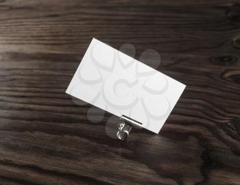 Photo of blank business card and paper clip on dark wooden background. White business card. Mock-up for branding identity. 