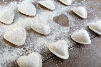 Cooking ravioli. Raw dumplings in the form of hearts sprinkled flour on wooden background closeup. Shallow depth of field.