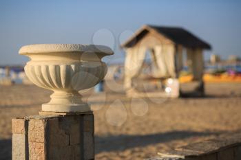 Old plaster vase in antique style on a background of a sandy beach and a canopy. Shallow depth of field.