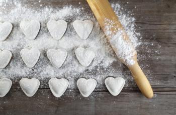 Cooking dumplings. Raw heart shaped dumplings, flour and rolling pin on wooden background. Top view.