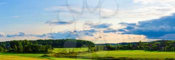 Rural landscape. Sunny summer evening. Sky with clouds, grass field, trees and farmhouses. Panoramic shot.
