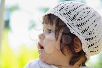 Baby in a white knitted cap outdoor close-up. Photo of a little girl in profile. Selective focus.