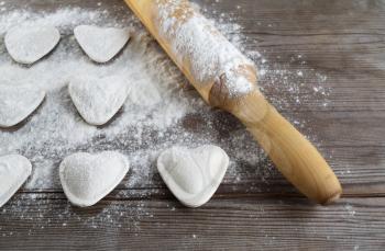 Raw heart shaped dumplings, flour and rolling pin on wooden background. Cooking ravioli. Shallow depth of field.