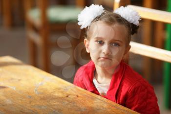 Portrait of a little girl in a red jacket with white bows on her head. Child sitting at the table. Shallow depth of field. Selective focus.