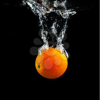 Orange falling into the water with a splash and air bubbles. Healthy food on black background. Wash fruits.