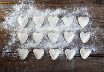 Heart shaped ravioli with flour, on vintage wood table background. Cooking dumplings. Top view.
