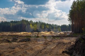 Sandy quarry in the pine forest. Scenic forest landscape and cloudy sky.