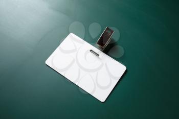 Blank white plastic badge on green chalkboard background. Empty ID card. Space for text. Template for branding identity.
