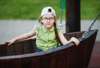 Girl in a baseball cap and glasses. Child on the playground. Selective focus.