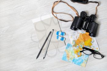 Ready for the trip. Travel plan background. Map, binoculars, notebook, glasses, pencils and flip flops on light wood table background. Flat lay.