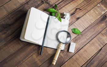 Photo of blank notebook, magnifier, pencil and eraser on wood table background.