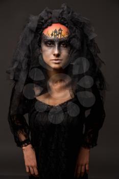 Halloween devil's bride. Portrait of young woman in dark artistic image with scary makeup, veil and terrible picture on her forehead.