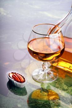Snifter of cognac with bottle and sweet on marple table