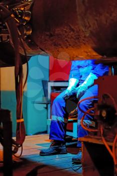 Welder resting during a break at work. Welding of the pipeline. Process of creation of welding connection by the special mobile machine. Worker sitting on a chair.
