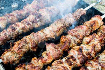 Frying pork on a skewer over a brazier. Turning meat over coals. Appetizing shish kebab. Delicious barbecue.