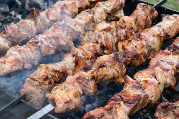 Frying pork on a skewer over a brazier. Turning meat over coals. Appetizing shish kebab. Delicious barbecue.