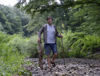 A man walks along the creek and carries wood for the fire. Picnic in nature. Harvesting of firewood.