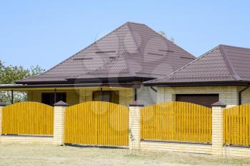 Brick house with corrugated metal profile roof and wooden fence. Beautiful view of the facade. Style of design.