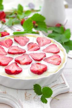 Delicious strawberry tart or cheesecake with fresh berries and cream cheese, closeup on white wooden rustic background