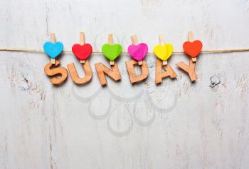 Sunday word from wooden letters with colored clothespins on a white wooden background