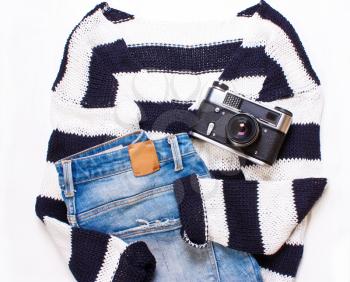 Sweater in white and blue stripes, jeans, and a camera.  Top view, flat.fashionable women's  casual clothes on a white background. Trendy hipster look, set