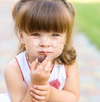 Little girl is eating chocolate candy, outdoor shoot
