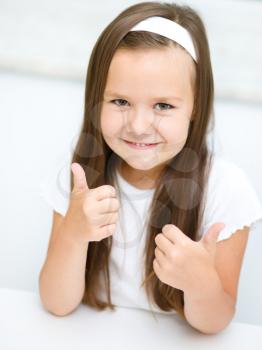 Little girl dressed in white is showing thumb up gesture using both hands